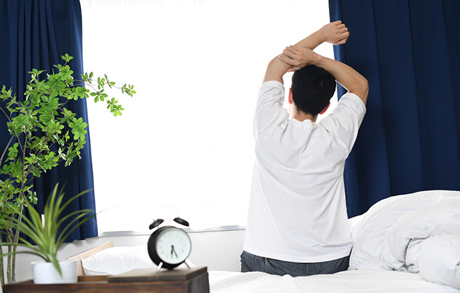 ベッドで背伸びする男性